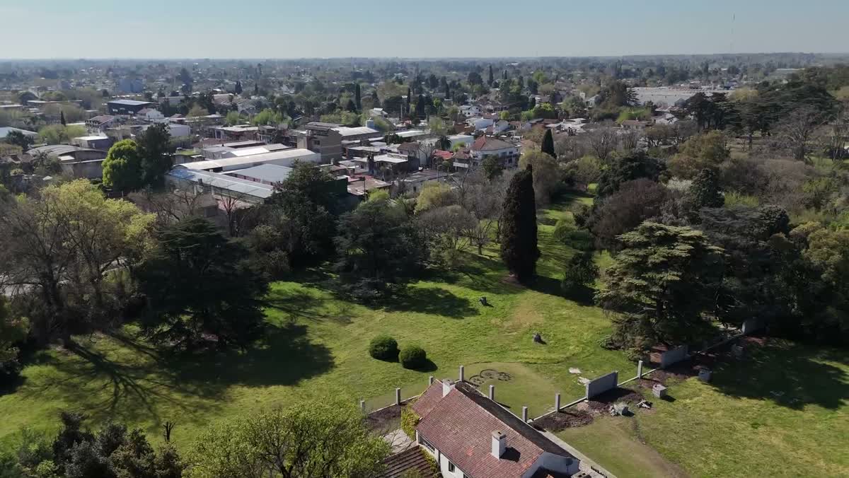 Vista aérea del parque de la finca, con árboles altos y la ciudad de Monte Grande de fondo